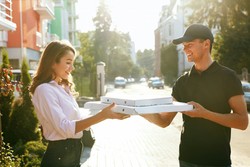 Pizza delivery person handing over pizza boxes to a smiling woman on a sunny street