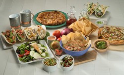 Cinco de Mayo party spread showcasing vibrant Mexican dishes: tacos stuffed with fresh vegetables, bowls of guacamole and salsa, rice garnished with tomatoes and herbs, crispy tortilla chips, and pizzas with creative toppings. The table features festive touches including metal shakers, sauce bottles, and colorful produce like tomatoes and avocados, all set on a clean white surface for a lively celebration.