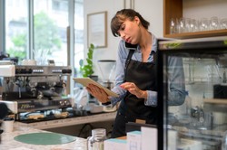 Manager managing reservations at a café using a tablet while talking on the phone.