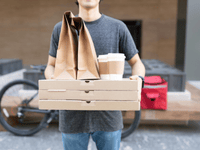 The image is a medium close-up of a food delivery person holding a substantial order.
