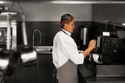 
This photograph shows a female chef operating a beverage machine in a professional kitchen.
