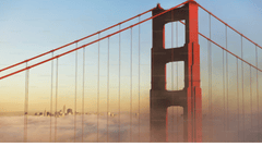 A close-up view of the Golden Gate Bridge tower painted in red, with suspension cables stretching diagonally across the frame.