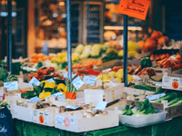 This image captures a colorful and well-stocked outdoor market stall filled with fresh fruits and vegetables. Crates display vibrant produce like zucchinis, bell peppers, tomatoes, leafy greens, and mushrooms, each labeled with handwritten price tags. The setup is warm, inviting, and authentic — perfect for communicating freshness and local sourcing.