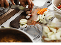 Person slicing vegetables on a clean cutting board during a food hygiene inspection to ensure proper kitchen safety standards.