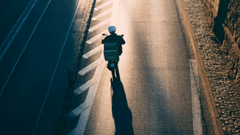The image presents an aerial view of a delivery person on a scooter, captured from behind as they travel down a road.