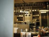 Industrial kitchen neatly arranged with hanging utensils, shelves holding plates, and stainless steel preparation equipment.