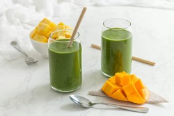Healthy green smoothies in cups with straws, accompanied by mango cubes on a table